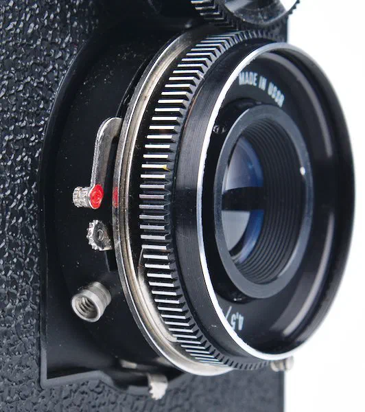 The lever to cock the shutter has a red dot. The shutter release is below it. The cable release socket is at the bottom. The lever to cock the shutter has a red dot. The shutter release is below it. The cable release socket is at the bottom.